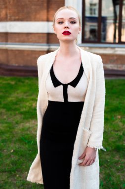 Mutlu moda sarışın Avrupa zarif kadın kırmızı dudakları ve beyaz ayakta yeşil çimenlerin üzerinde bina eski kırmızı tuğla, Cilt. Seksi kız açık havada. Resmi siyah beyaz elbiseli güzel kadın.