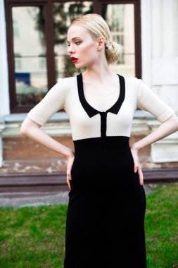 Mutlu moda sarışın Avrupa zarif kadın kırmızı dudakları ve beyaz ayakta yeşil çimenlerin üzerinde bina eski kırmızı tuğla, Cilt. Seksi kız açık havada. Resmi siyah beyaz elbiseli güzel kadın.