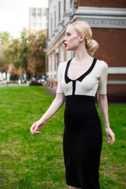 Mutlu moda sarışın Avrupa zarif kadın kırmızı dudakları ve beyaz ayakta yeşil çimenlerin üzerinde bina eski kırmızı tuğla, Cilt. Seksi kız açık havada. Resmi siyah beyaz elbiseli güzel kadın.