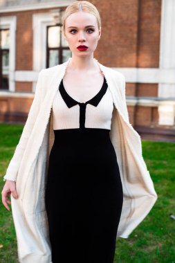 Mutlu moda sarışın Avrupa zarif kadın kırmızı dudakları ve beyaz ayakta yeşil çimenlerin üzerinde bina eski kırmızı tuğla, Cilt. Seksi kız açık havada. Resmi siyah beyaz elbiseli güzel kadın.