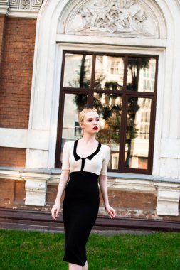 Mutlu moda sarışın Avrupa zarif kadın kırmızı dudakları ve beyaz ayakta yeşil çimenlerin üzerinde bina eski kırmızı tuğla, Cilt. Seksi kız açık havada. Resmi siyah beyaz elbiseli güzel kadın.