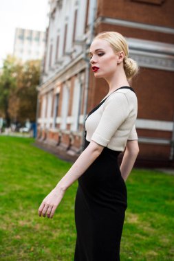 Mutlu moda sarışın Avrupa zarif kadın kırmızı dudakları ve beyaz ayakta yeşil çimenlerin üzerinde bina eski kırmızı tuğla, Cilt. Seksi kız açık havada. Resmi siyah beyaz elbiseli güzel kadın.