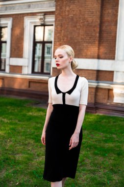 Mutlu moda sarışın Avrupa zarif kadın kırmızı dudakları ve beyaz ayakta yeşil çimenlerin üzerinde bina eski kırmızı tuğla, Cilt. Seksi kız açık havada. Resmi siyah beyaz elbiseli güzel kadın.