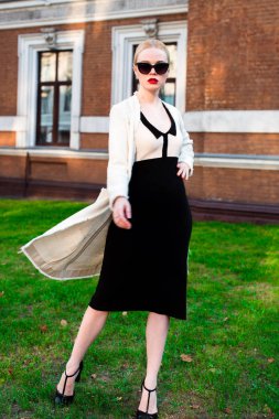 Mutlu moda sarışın Avrupa zarif kadın kırmızı dudakları ve beyaz ayakta yeşil çimenlerin üzerinde bina eski kırmızı tuğla, Cilt. Seksi kız açık havada. Resmi siyah beyaz elbiseli güzel kadın 