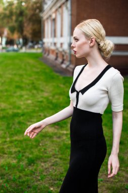 Mutlu moda sarışın Avrupa zarif kadın kırmızı dudakları ve beyaz ayakta yeşil çimenlerin üzerinde bina eski kırmızı tuğla, Cilt. Seksi kız açık havada. Resmi siyah beyaz elbiseli güzel kadın.