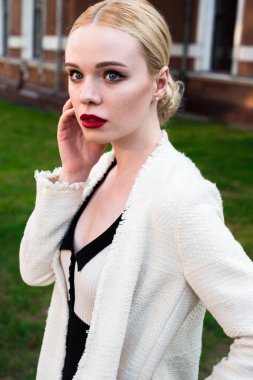 Mutlu moda sarışın Avrupa zarif kadın kırmızı dudakları ve beyaz ayakta yeşil çimenlerin üzerinde bina eski kırmızı tuğla, Cilt. Seksi kız açık havada. Resmi siyah beyaz elbiseli güzel kadın.