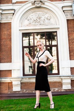 Mutlu moda sarışın Avrupa zarif kadın kırmızı dudakları ve beyaz ayakta yeşil çimenlerin üzerinde bina eski kırmızı tuğla, Cilt. Seksi kız açık havada. Resmi siyah beyaz elbiseli güzel kadın.