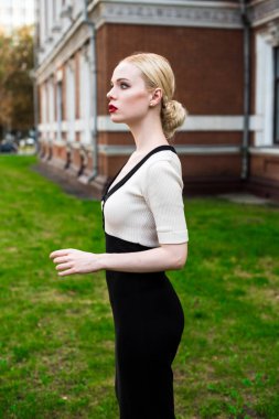 Mutlu moda sarışın Avrupa zarif kadın kırmızı dudakları ve beyaz ayakta yeşil çimenlerin üzerinde bina eski kırmızı tuğla, Cilt. Seksi kız açık havada. Resmi siyah beyaz elbiseli güzel kadın.