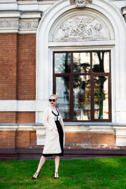 Mutlu moda sarışın Avrupa zarif kadın kırmızı dudakları ve beyaz ayakta yeşil çimenlerin üzerinde bina eski kırmızı tuğla, Cilt. Seksi kız açık havada. Resmi siyah beyaz elbiseli güzel kadın 