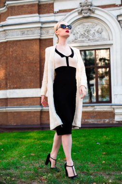 Mutlu moda sarışın Avrupa zarif kadın kırmızı dudakları ve beyaz ayakta yeşil çimenlerin üzerinde bina eski kırmızı tuğla, Cilt. Seksi kız açık havada. Resmi siyah beyaz elbiseli güzel kadın 