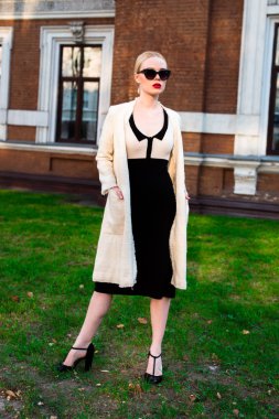 Mutlu moda sarışın Avrupa zarif kadın kırmızı dudakları ve beyaz ayakta yeşil çimenlerin üzerinde bina eski kırmızı tuğla, Cilt. Seksi kız açık havada. Resmi siyah beyaz elbiseli güzel kadın 