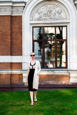 Mutlu moda sarışın Avrupa zarif kadın kırmızı dudakları ve beyaz ayakta yeşil çimenlerin üzerinde bina eski kırmızı tuğla, Cilt. Seksi kız açık havada. Resmi siyah beyaz elbiseli güzel kadın 