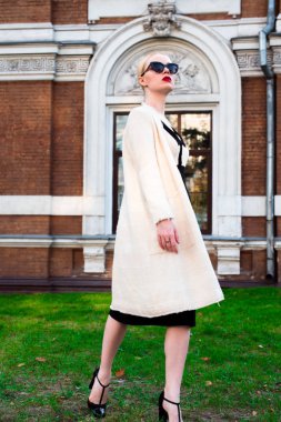 Mutlu moda sarışın Avrupa zarif kadın kırmızı dudakları ve beyaz ayakta yeşil çimenlerin üzerinde bina eski kırmızı tuğla, Cilt. Seksi kız açık havada. Resmi siyah beyaz elbiseli güzel kadın 