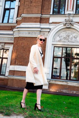 Mutlu moda sarışın Avrupa zarif kadın kırmızı dudakları ve beyaz ayakta yeşil çimenlerin üzerinde bina eski kırmızı tuğla, Cilt. Seksi kız açık havada. Resmi siyah beyaz elbiseli güzel kadın 