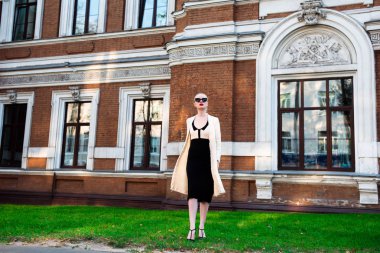 Mutlu moda sarışın Avrupa zarif kadın kırmızı dudakları ve beyaz ayakta yeşil çimenlerin üzerinde bina eski kırmızı tuğla, Cilt. Seksi kız açık havada. Resmi siyah beyaz elbiseli güzel kadın 