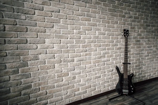 The guitar stands near the stone wall