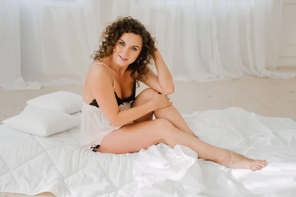 Sexy woman in bed in the morning showing her beautiful body. She doesn\'t wants to wake up. Awaken with natural light in her bedroom and covered with the bed sheets.