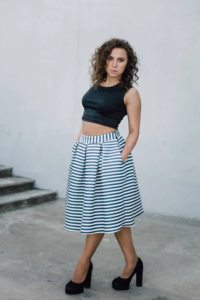 Uzun dalgalı saçlı güzel seksi genç esmer kız ince ince şekil ve oldukça uzun soyulmuş bir etek ve siyah bluz, yüksek topuklu giyiyor makyaj yüz. Rahat tarzı sokakta yürümek