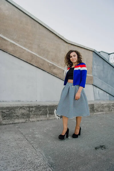 Mooie sexy jonge brunette meisje met lang golvend haar slanke figuur dun en mooi gezicht make-up dragen van een lange gestripte rok en zwarte top, hoge hakken. Lopen op straat in casual stijl — Stockfoto