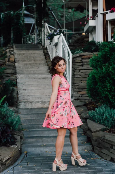 Menina morena bonita posando em vestido rosa fora perto de plantas tropicais — Fotografia de Stock