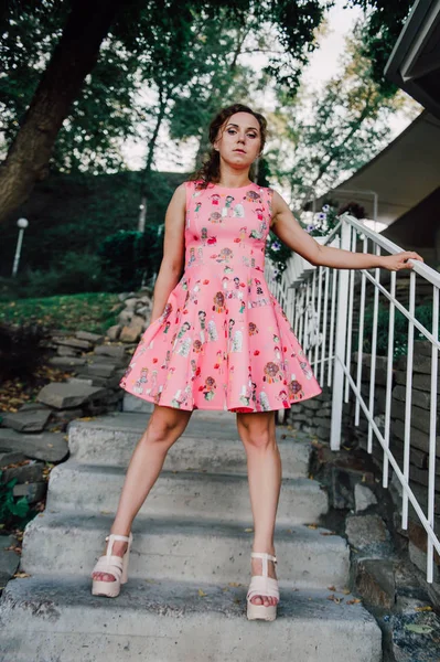 Menina morena bonita posando em vestido rosa fora perto de plantas tropicais — Fotografia de Stock