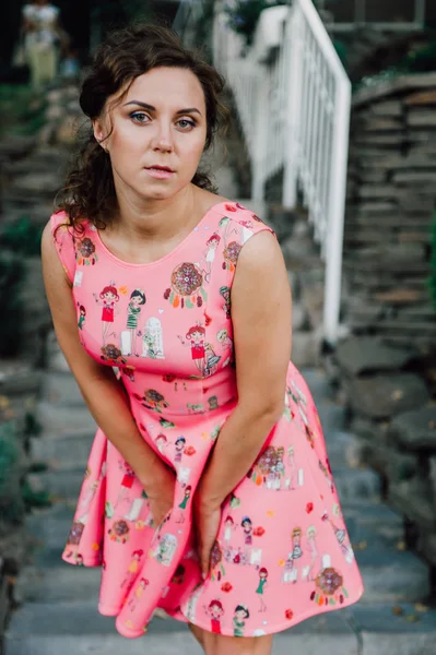 Hermosa chica morena posando en vestido rosa afuera cerca de plantas tropicales —  Fotos de Stock