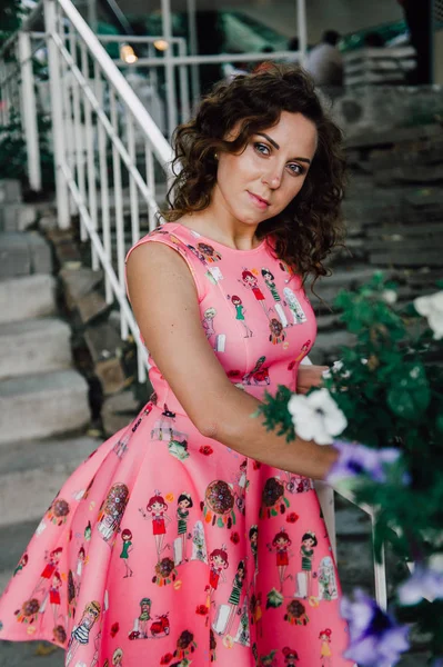 Mooie brunette meisje poseren in roze jurk buiten in de buurt van tropische planten — Stockfoto