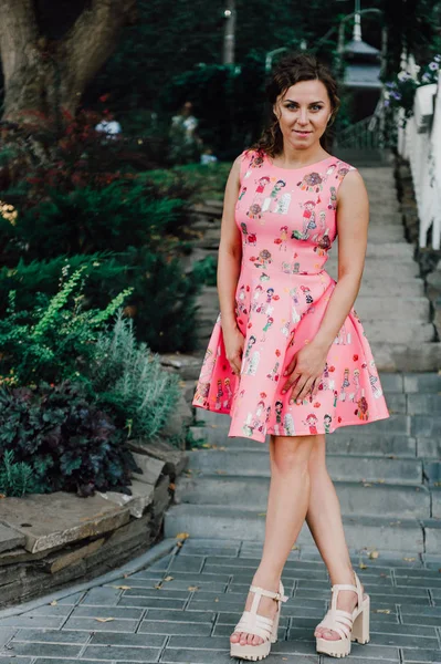 Menina morena bonita posando em vestido rosa fora perto de plantas tropicais — Fotografia de Stock