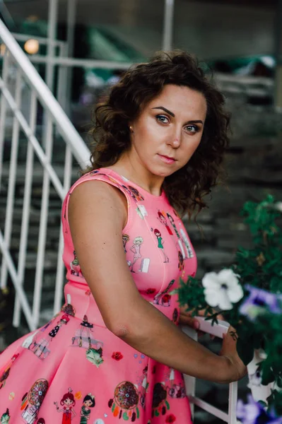 Hermosa chica morena posando en vestido rosa afuera cerca de plantas tropicales —  Fotos de Stock