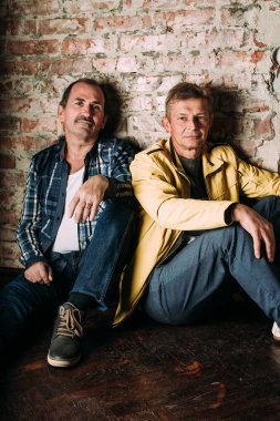 Casual kılığına girmiş iki yakışıklı orta yaşlı erkekler, eski dostlar. Kırmızı tuğla duvar arka plan.