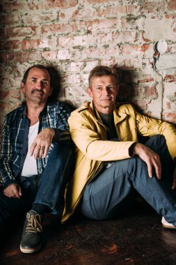 Casual kılığına girmiş iki yakışıklı orta yaşlı erkekler, eski dostlar. Kırmızı tuğla duvar arka plan.