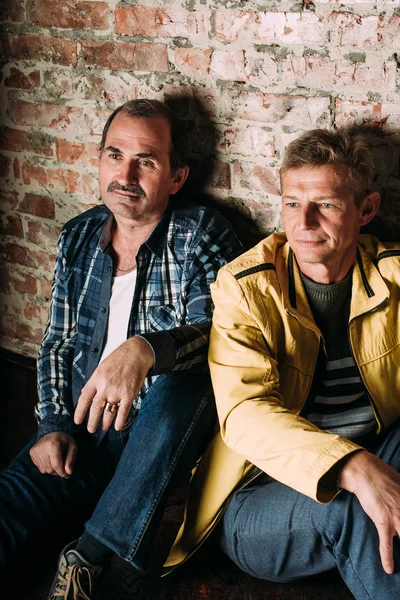 Dos hombres guapos de mediana edad, vestidos con ropa casual, viejos amigos. Fondo de pared de ladrillo rojo . — Foto de Stock