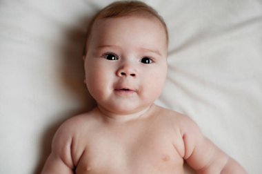 Beyaz yatağa uzanmış güzel bir erkek bebeğin yumuşak bir resmi.