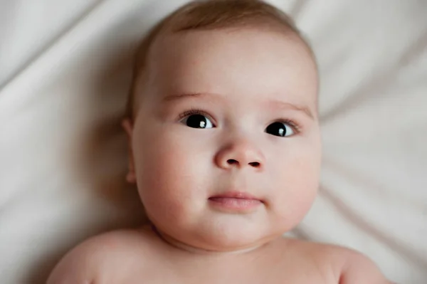 Soft picture of a beautiful baby boy laying on white bedding — Stock Photo, Image