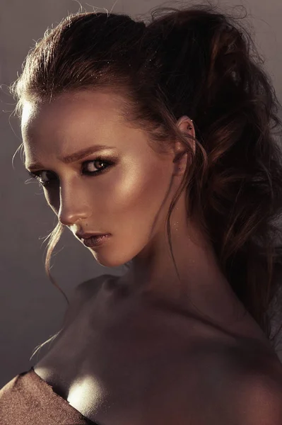 Αίγλη πορτρέτο της μόδας της νεανικής μόδας γυναίκα πρόσωπο με χρυσή φωτεινό βράδυ συνθέτουν για πάρτι και μαυρισμένο δέρμα. Ζεστό χρωματικό τόνο. Retouched κοντά επάνω πορτρέτο — Φωτογραφία Αρχείου
