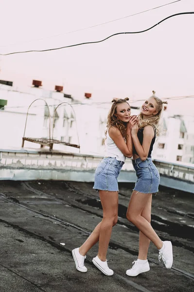 Lifestyle and people concept: Fashion portrait of two stylish girls best friends wearing jeans skirts, outdoors on the roof. Happy summer time for fun. Concept of 90s. Retouched photo — Stock Photo, Image