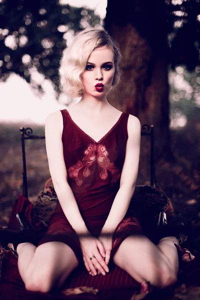 Vacker och elegant blond kvinna med röda läppar och hår vinkar bär vin rött nattlinne poserar på sängen utomhus höst, retro vintage stil och mode. Retuscheras toning skott — Stockfoto
