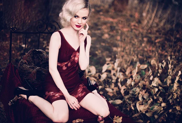 Mooi en elegant blonde vrouw met rode lippen en haren golven dragen wijn rode nachtjapon poseren op het bed buitenshuis herfst, retro vintage stijl en mode. Geretoucheerd toning schot — Stockfoto