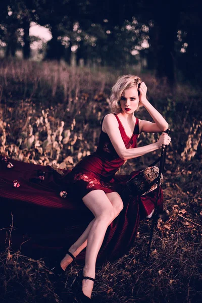 Piękna i elegancka blond kobieta z czerwonymi ustami i włosów fale noszenia wina czerwonej koszuli nocnej pozowanie na łóżku na zewnątrz, jesień, retro styl vintage i mody. Retuszować, tonowanie strzał — Zdjęcie stockowe