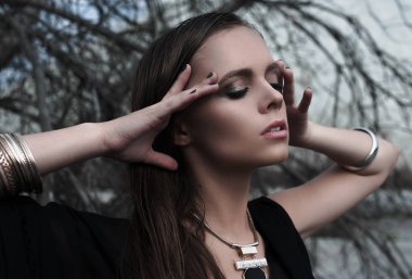 Güzel esmer kız parlak makyaj ve mor dudak siyah açık havada mavi yaz göğün üzerinde poz giyiyor. Düzeltisiz atış. Yakın, güzellik potrtait