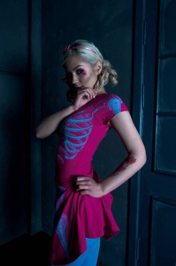 Yaratıcı bebek makyaj ile iki kuyruklu ile güzel sarışın kız: pembe Pembe iskelet elbise, kapının yanında poz parlak dudaklar. Cadılar Bayramı partisi için. Bir bebek gibi poz. Atış, reto stüdyo