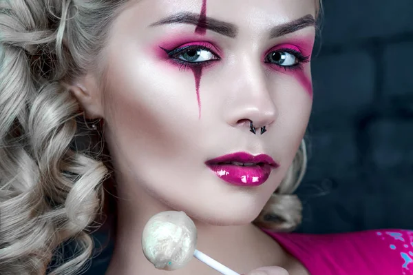 Mooie blonde meisje met twee pigtails, met creatieve pop make-up: roze glanzend lippen, het dragen van roze skelet jurk likken lollipop. voor de Halloween-party. Close-up, geretoucheerde foto. — Stockfoto