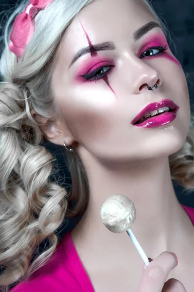 Beautiful blonde girl with two pigtails, with creative doll make-up: pink glossy lips, wearing pink skeleton dress licking lollipop. for the Halloween party. Close up, retouched image. — Stock Photo, Image
