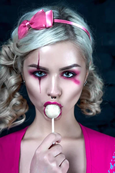 Mooie blonde meisje met twee pigtails, met creatieve pop make-up: roze glanzend lippen, het dragen van roze skelet jurk likken lollipop. voor de Halloween-party. Close-up, geretoucheerde foto. — Stockfoto