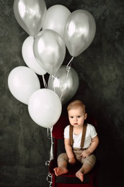 Portre sevimli küçük çocuk gülümseyen kutluyor 1 yıl kutlu olsun. Bir sandalyede oturuyor ve baloons ile oynarken bir yıl eski Avrupa küçük beyefendi