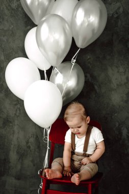 Portre sevimli küçük çocuk gülümseyen kutluyor 1 yıl kutlu olsun. Bir sandalyede oturuyor ve baloons ile oynarken bir yıl eski Avrupa küçük beyefendi