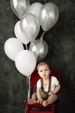 Portre sevimli küçük çocuk gülümseyen kutluyor 1 yıl kutlu olsun. Bir sandalyede oturuyor ve baloons ile oynarken bir yıl eski Avrupa küçük beyefendi