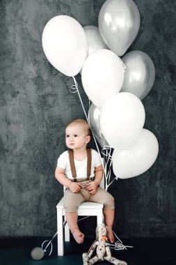 Portre sevimli küçük çocuk gülümseyen kutluyor 1 yıl kutlu olsun. Bir sandalyede oturuyor ve baloons ile oynarken bir yıl eski Avrupa küçük beyefendi
