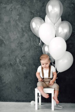Portre sevimli küçük çocuk gülümseyen kutluyor 1 yıl kutlu olsun. Bir sandalyede oturuyor ve baloons ile oynarken bir yıl eski Avrupa küçük beyefendi