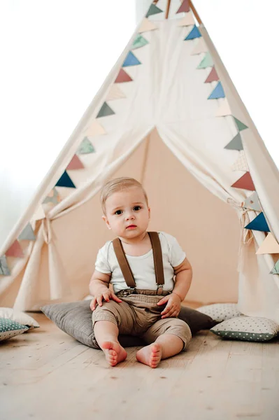 Retrato de adorável menino pequeno feliz sorrindo celebrando 1 ano de aniversário. Um ano de idade europeu pequeno cavalheiro sentado em uma tenda de bebê wigwam — Fotografia de Stock